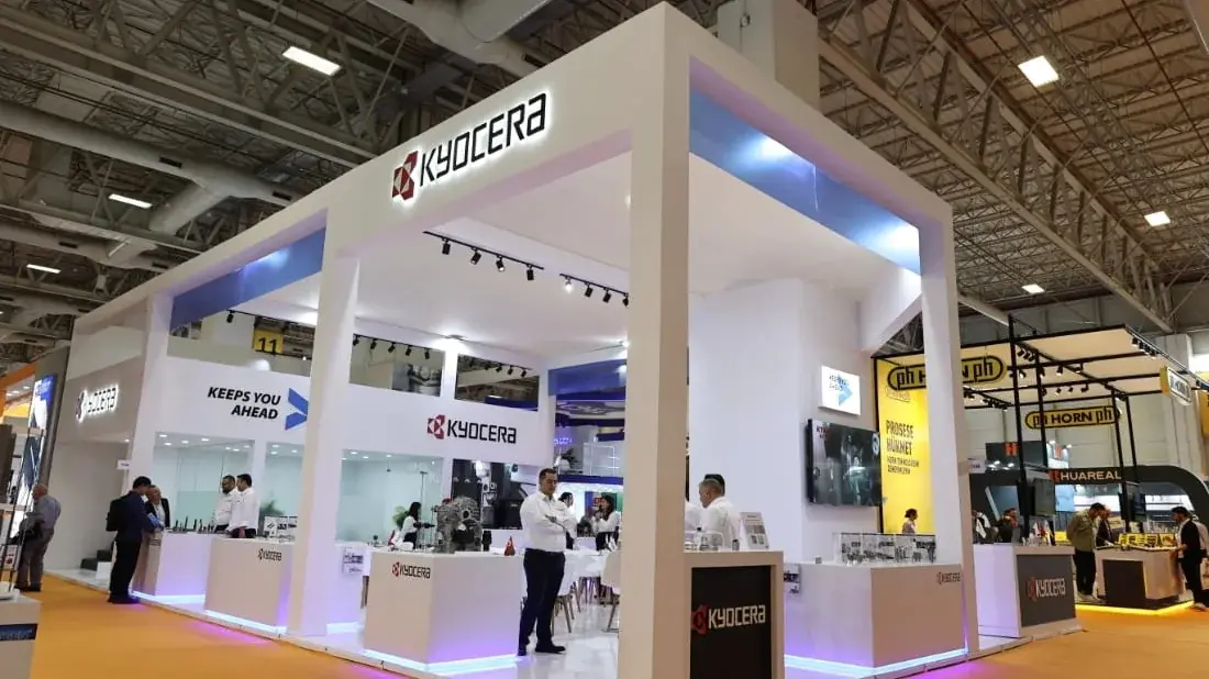 Kyocera için kurulan dört cepheli beyaz ada stand, asma tavanlı ve ışıklı alın kuşağıyla